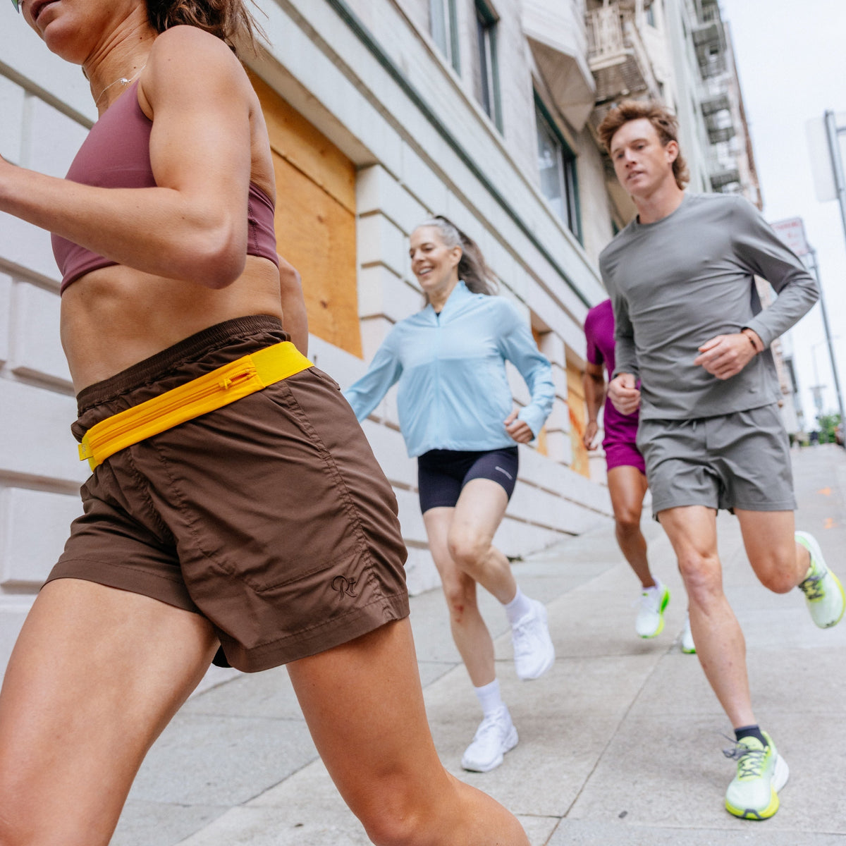 Men and women in a run group running along the street in athletic apparel and running shoes.